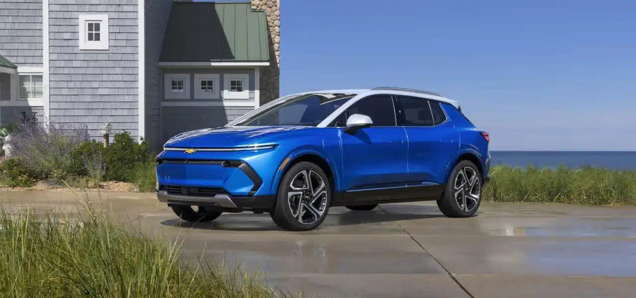 Blue electric SUV parked by a coastal house, showcasing modern design and eco-friendly features.