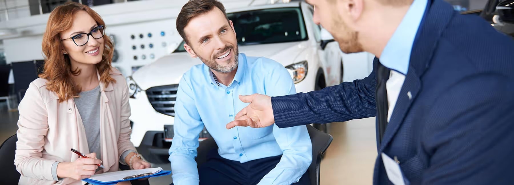 Car dealership consultation, smiling couple discussing car purchase options with salesman inside showroom.