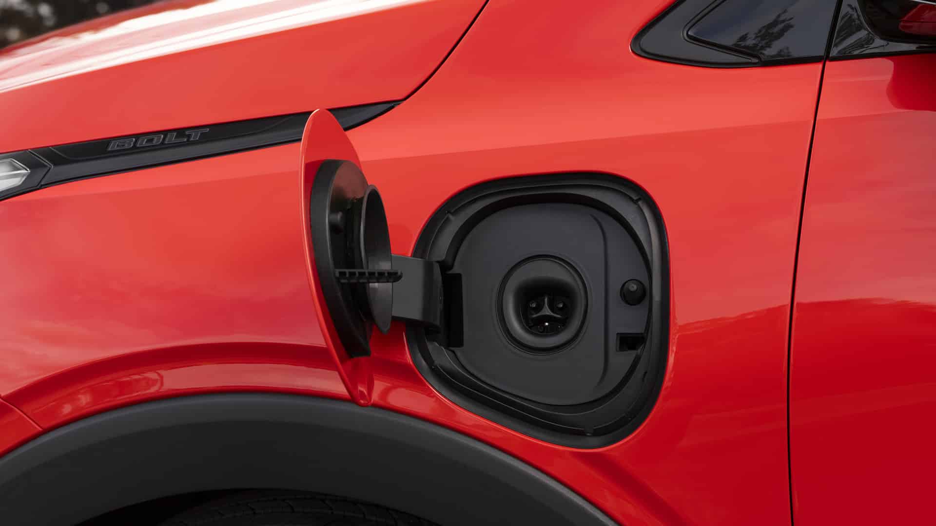 Electric car charging port on a red vehicle, viewed from a side angle.