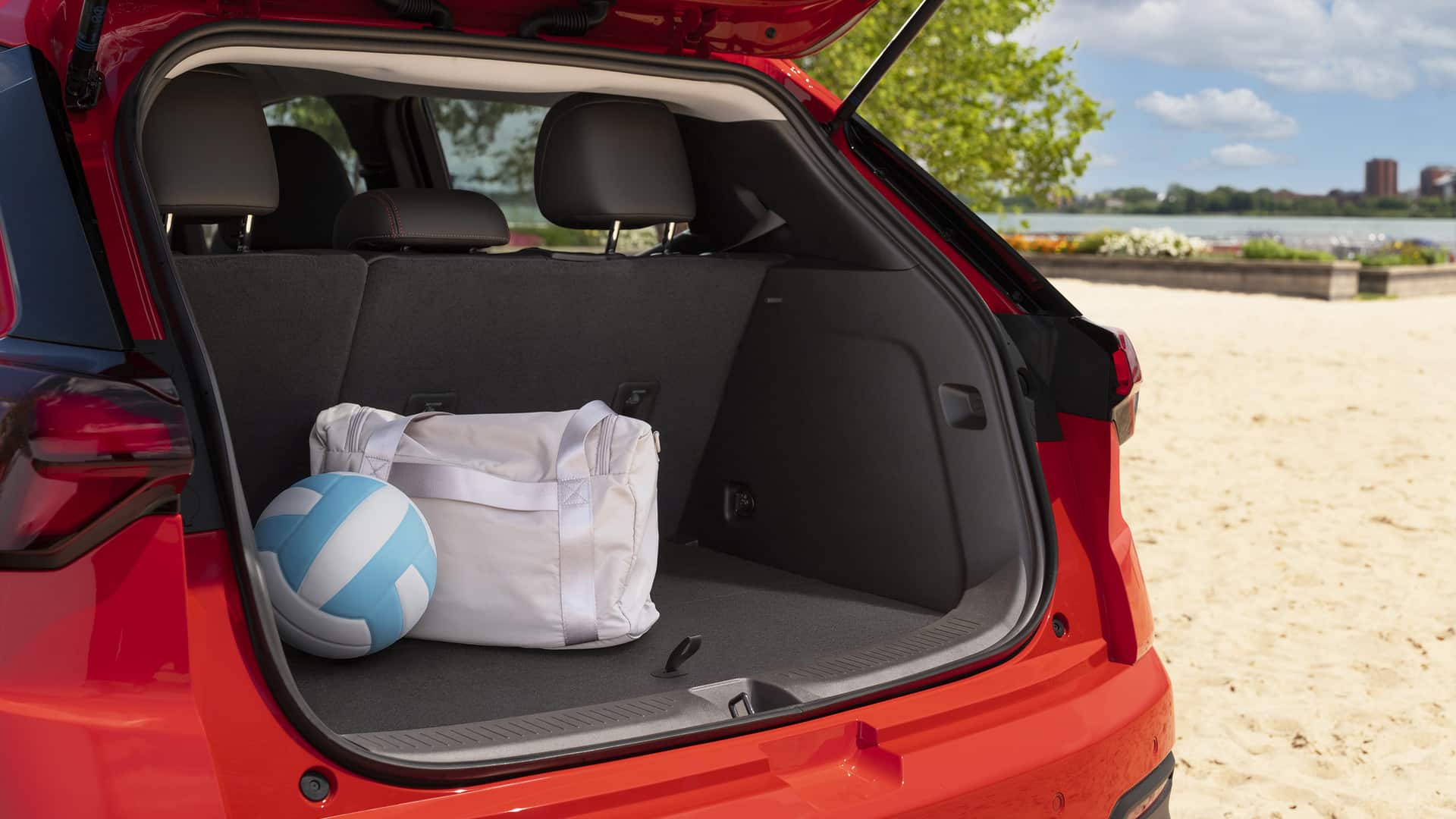 Open car trunk at beach with a volleyball and white duffel bag inside. Bright, sandy setting.