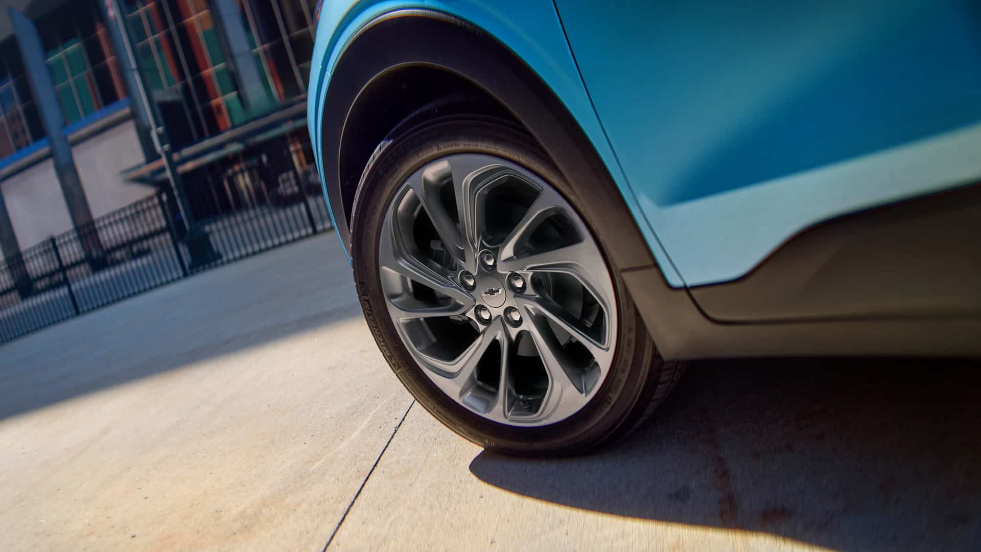 Close-up of a modern car's alloy wheel with a sleek, blue body, parked on a sunlit pavement.