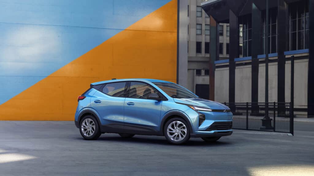 A blue electric vehicle parked in front of a vibrant wall featuring blue and orange diagonal sections.