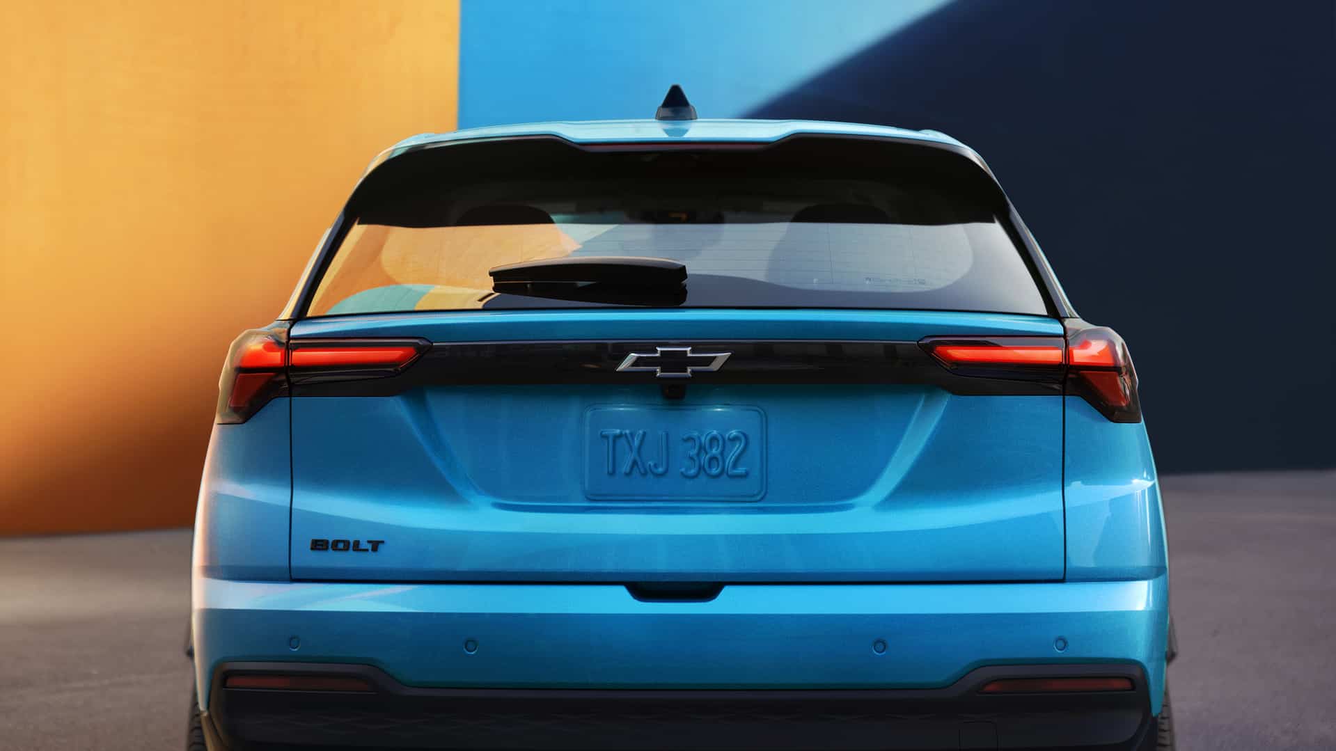 Rear view of a blue Chevrolet Bolt EV against a vibrant yellow and blue background.