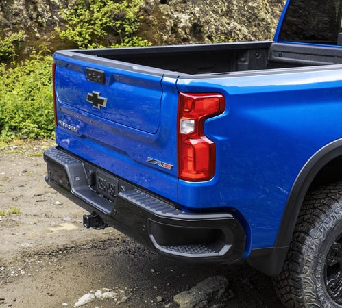Blue truck parked on rocky terrain, showcasing the open cargo bed and tailgate with brand logo.