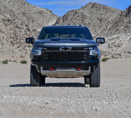 A black pickup truck with rugged terrain and rocky mountains in the background.