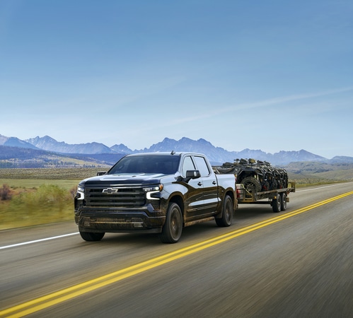 Chevrolet Silverado towing a trailer on an open road with mountains in the background.