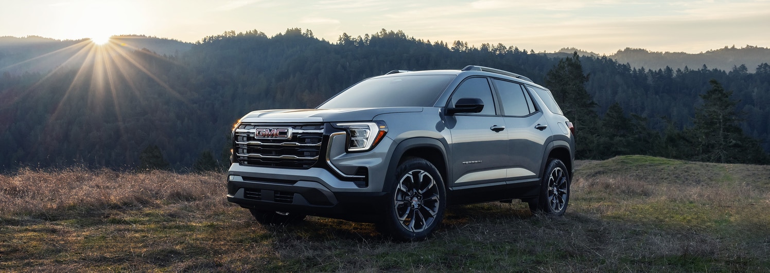 A shiny red SUV is parked in a dimly lit urban setting at night. The car features a sleek design with distinctive wheel rims, and illuminated headlights, reflecting light on the wet pavement. Modern architectural elements are visible in the background.
