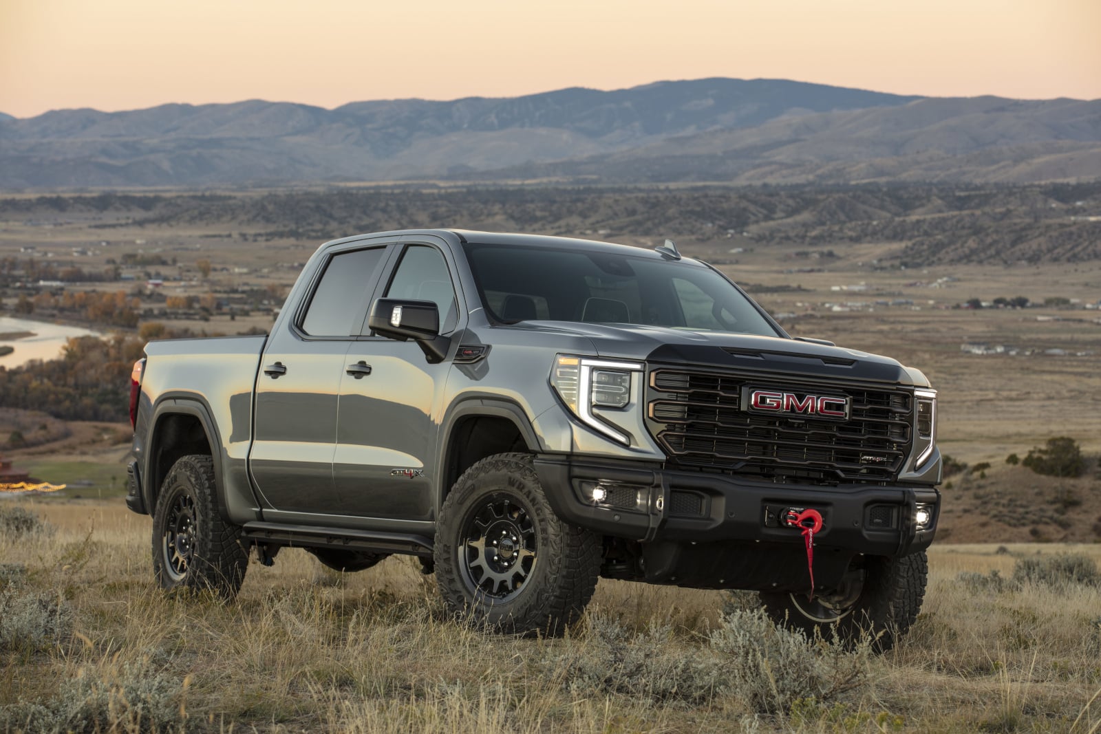 Silver GMC pickup truck on a grassy field with mountains under a sunset sky.