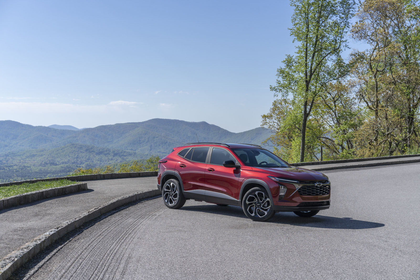 Red SUV parked on a scenic mountain road with lush greenery and blue sky in the background.
