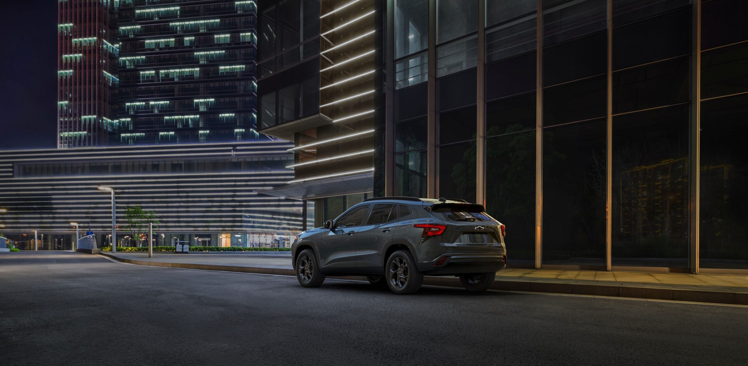 SUV parked on a modern city street at night, with illuminated skyscraper in the background.